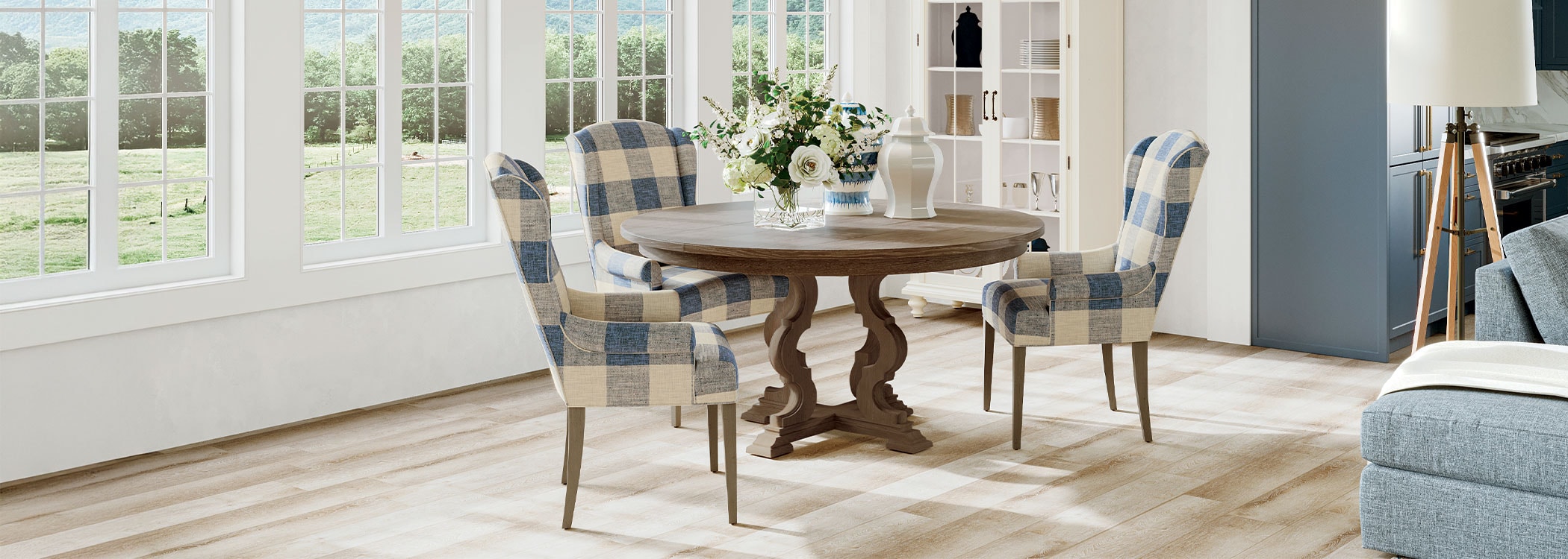 Bright dining room with round wooden table, plaid chairs, and large windows