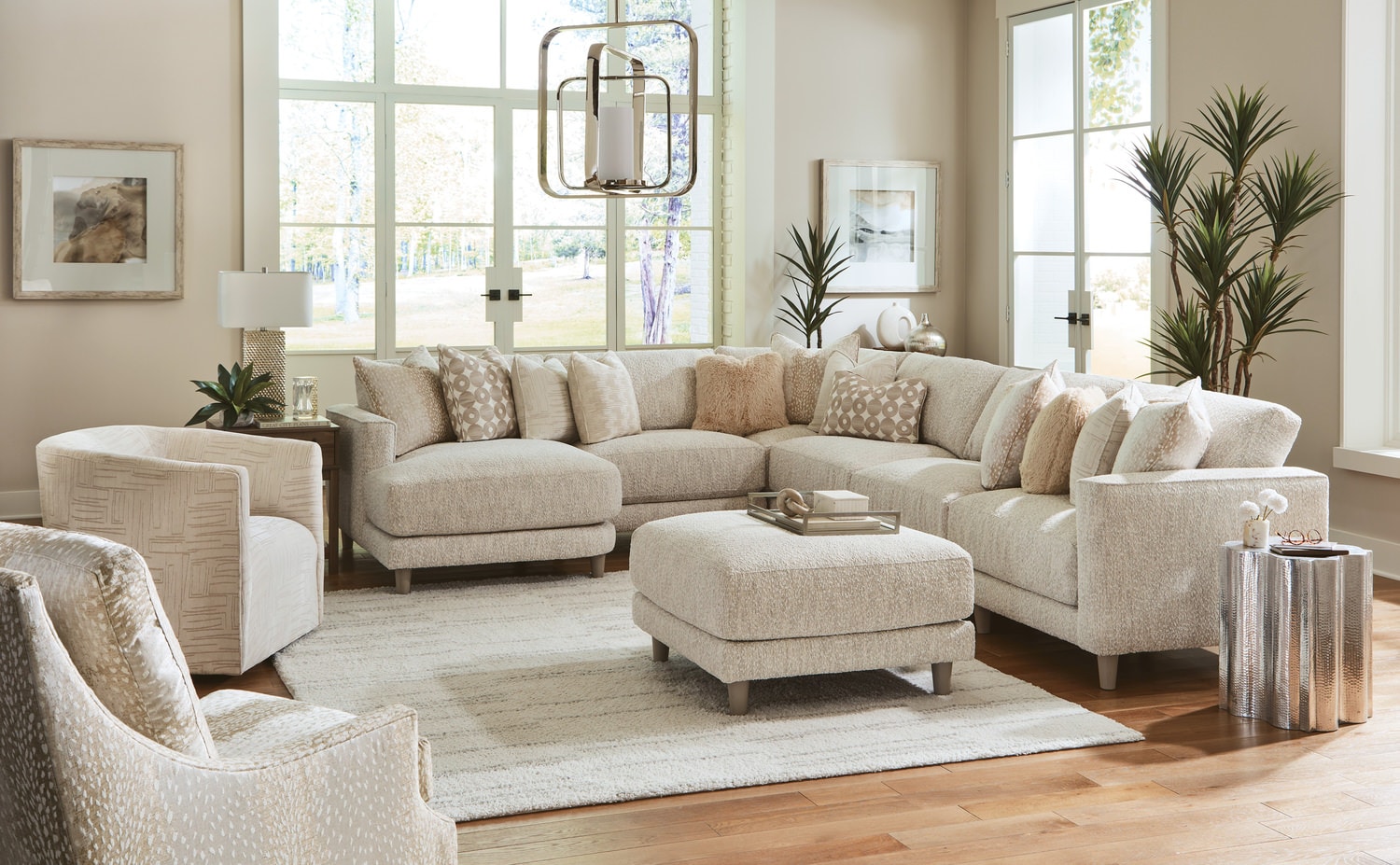 Elegant living room with neutral-toned sectional sofa, armchairs, and ottoman set on a beige rug, with large windows