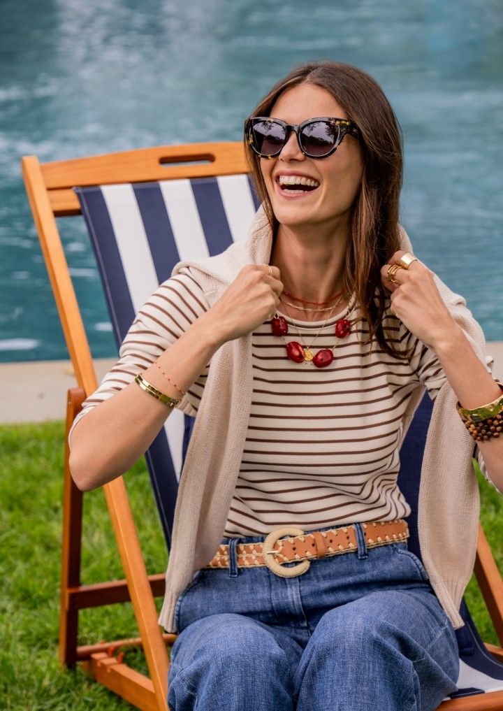 Woman smiling in sunglasses, sitting in a deck chair by water