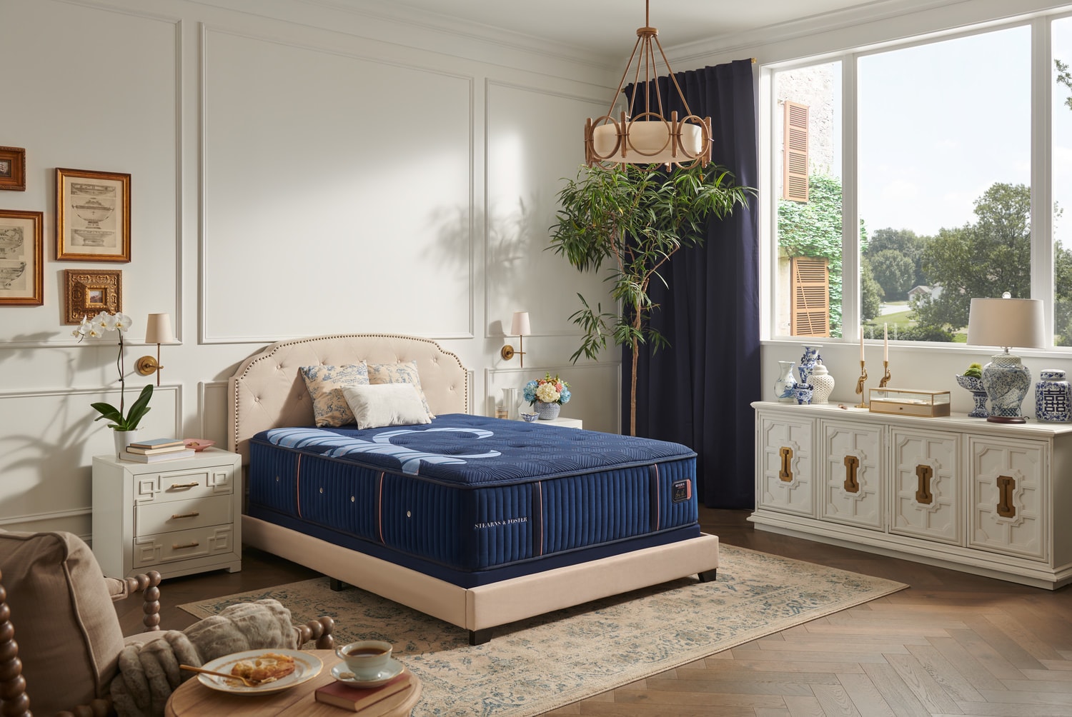 Elegant bedroom with a beige bed, navy blue bedding, white cabinets, and a cozy sitting area by a window