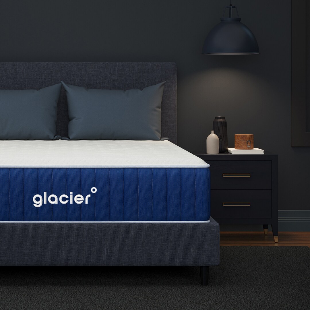 A modern bedroom with a Glacier mattress on a bed frame, beside a black nightstand under a hanging lamp