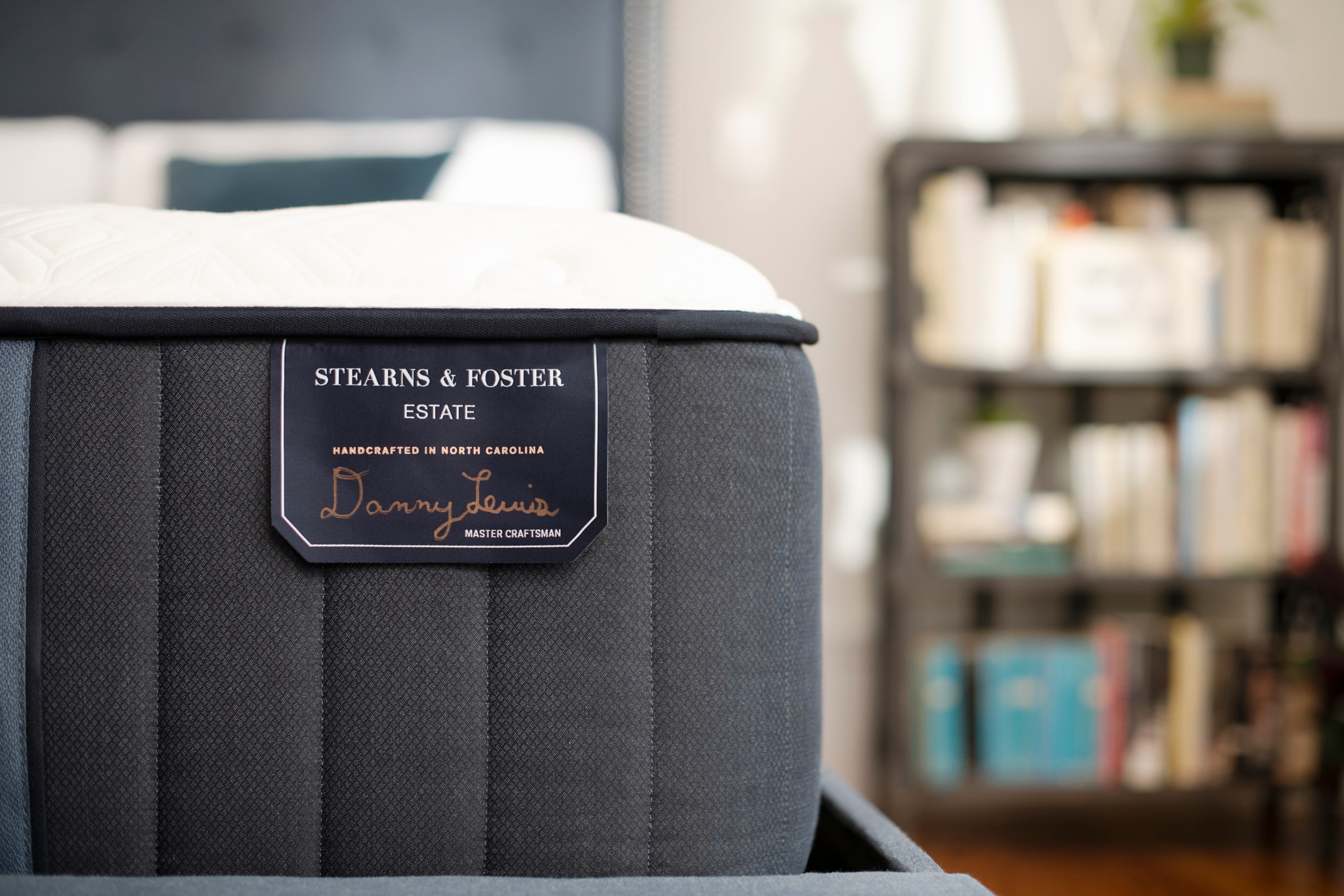 Close-up of a Stearns & Foster mattress corner tag, blurred bookshelf background