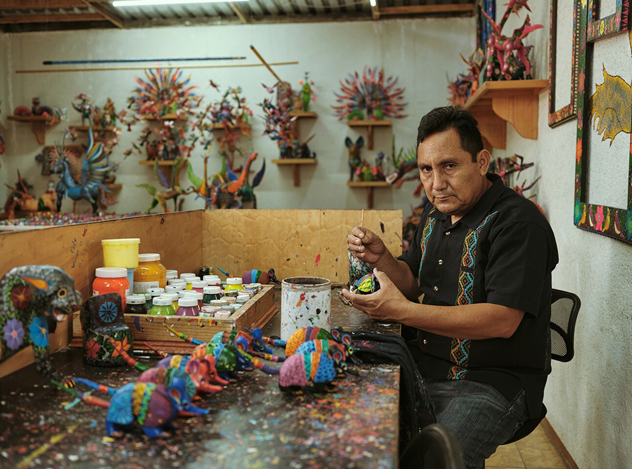 Man crafting colorful alebrijes in a workshop surrounded by finished pieces