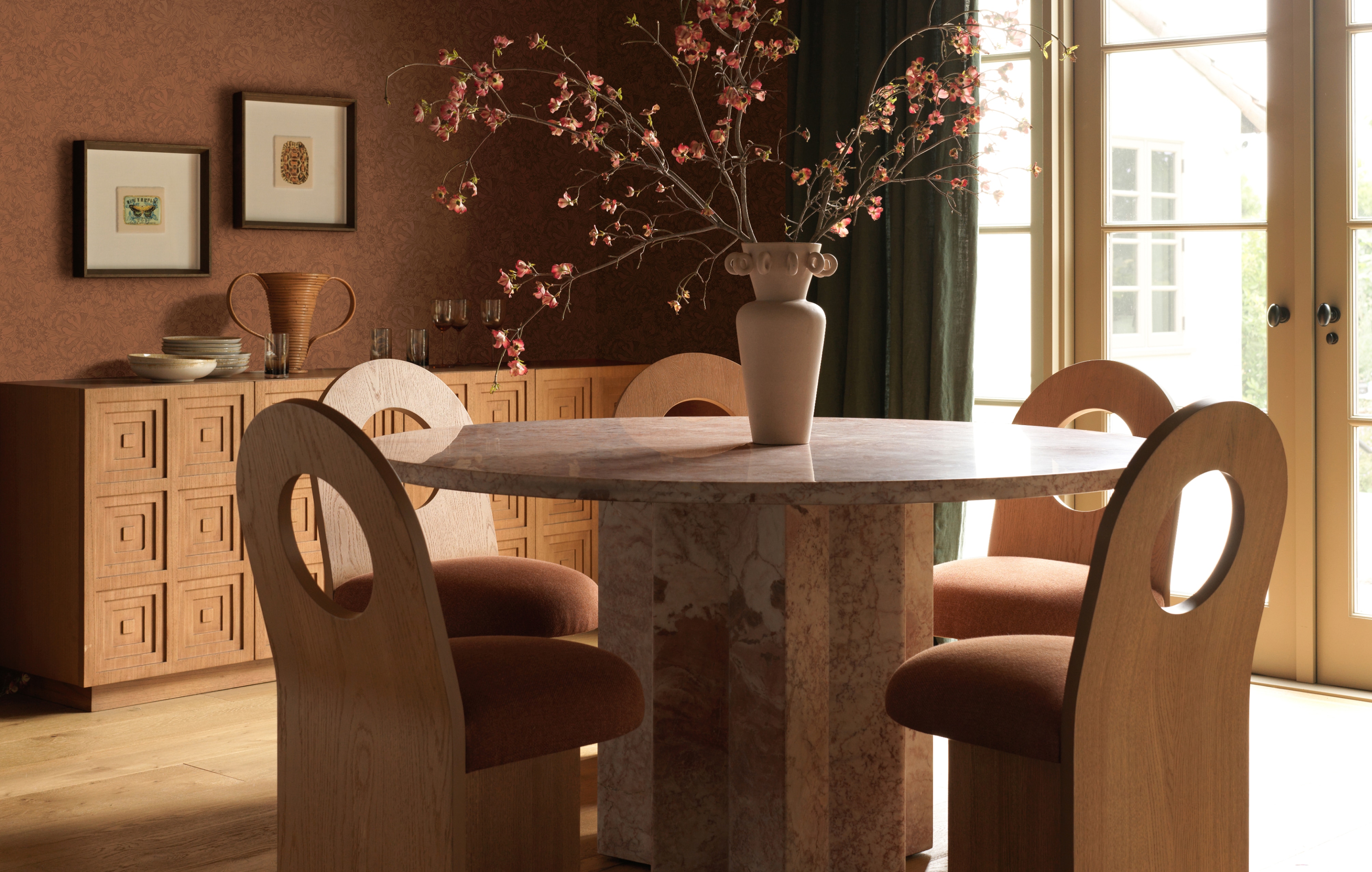 Modern dining room with round marble table, plush chairs, and a floral centerpiece in a warmly lit interior