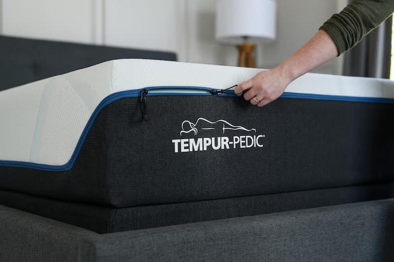 Hand adjusting a Tempur-Pedic mattress with visible logo on the side