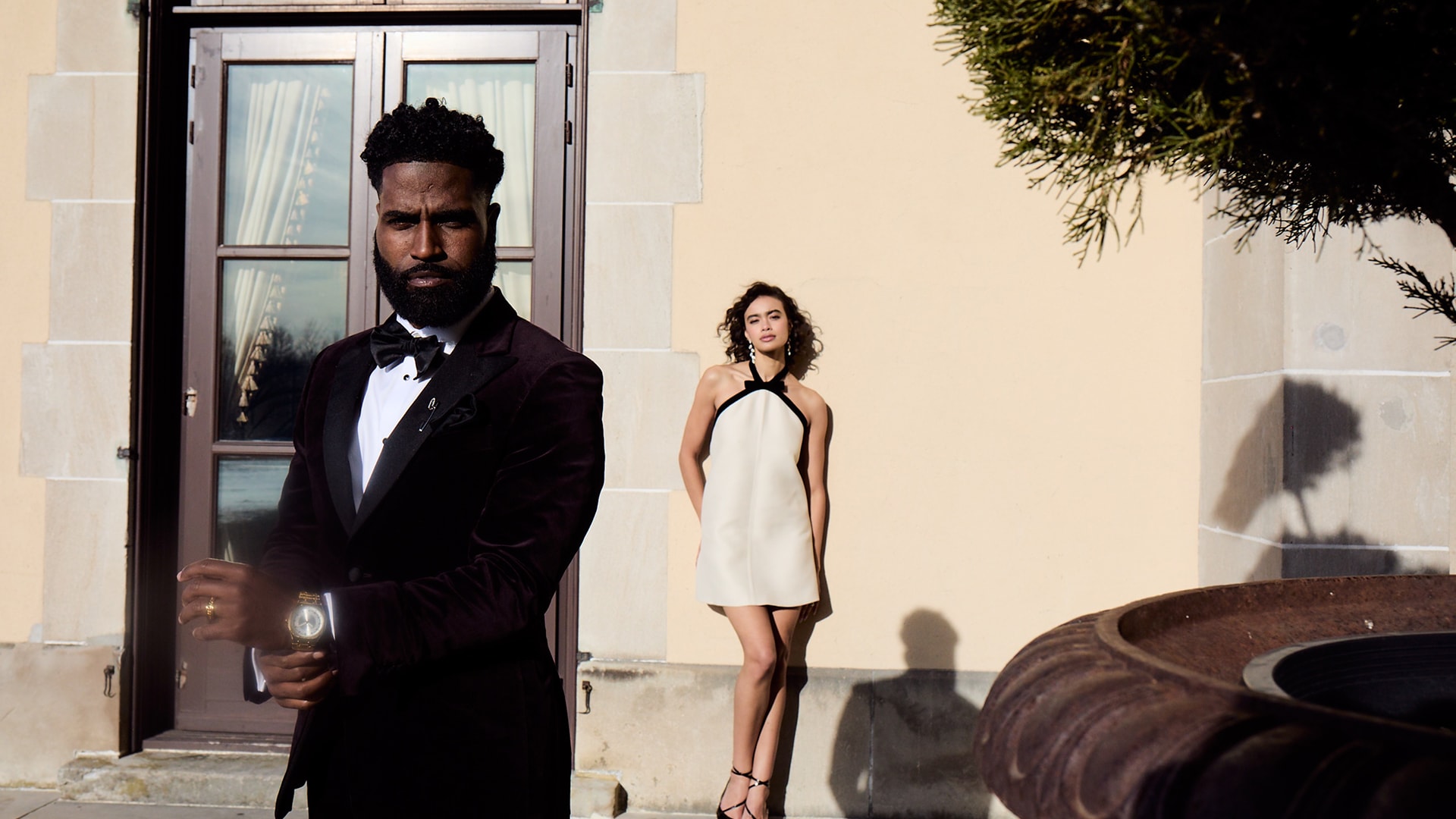 Man in tuxedo and woman in white dress standing by a building entrance