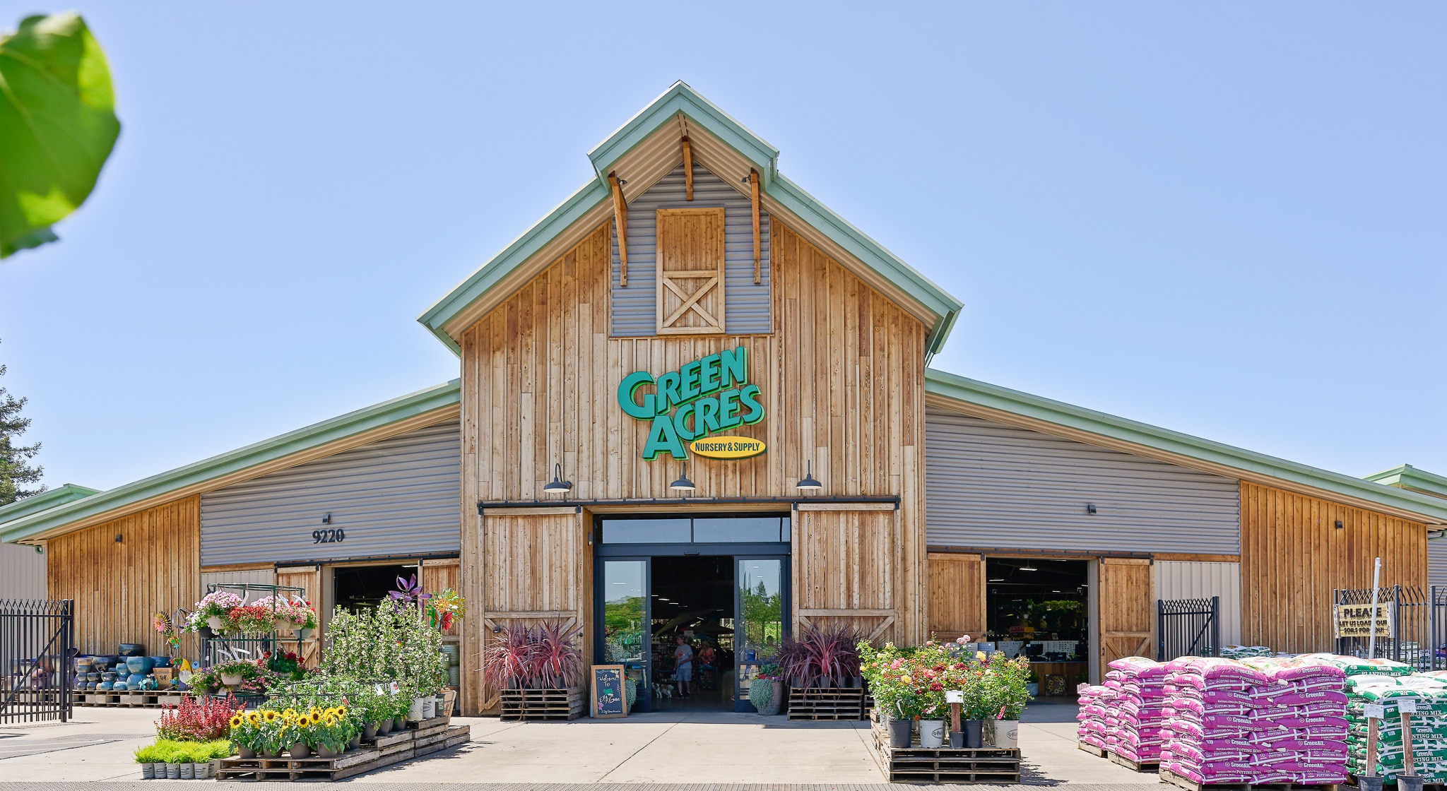 Front view of a rustic Green Acres Garden Center building with planting supplies displayed outside