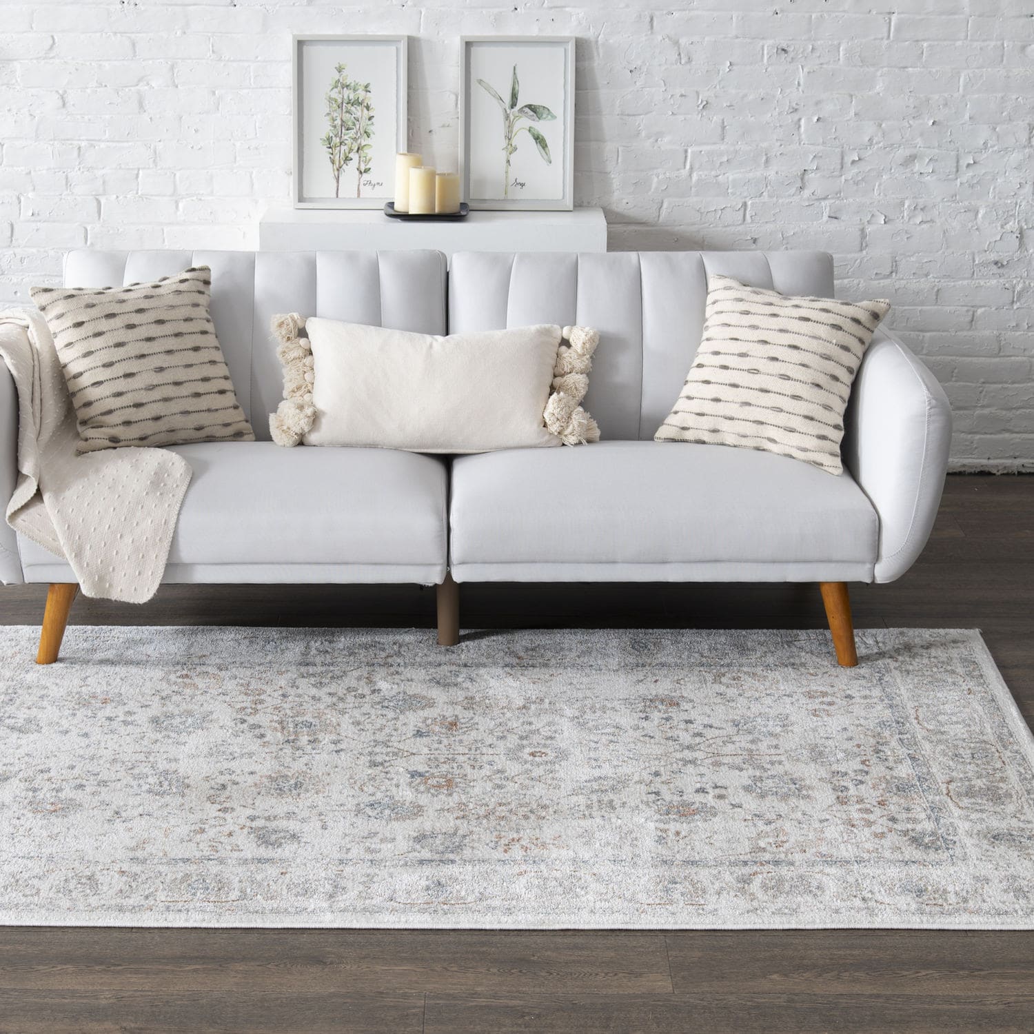 A modern gray sofa with cushions, set against a white brick wall with two framed botanical prints above it