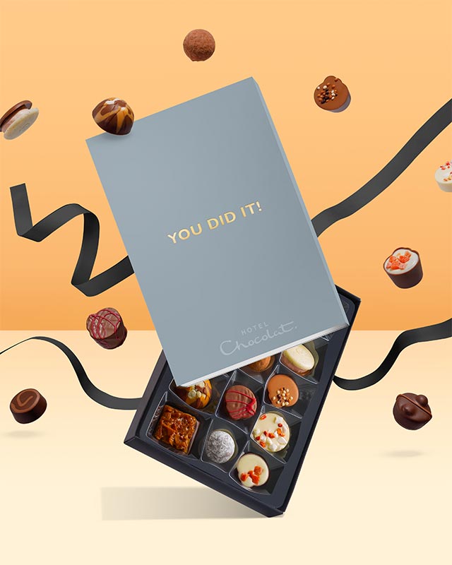 Box of chocolates with "You Did It!" card, floating among scattered candies on an orange background