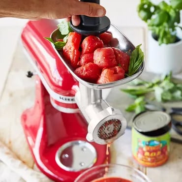 Red kitchen mixer with a meat grinder attachment processing tomatoes