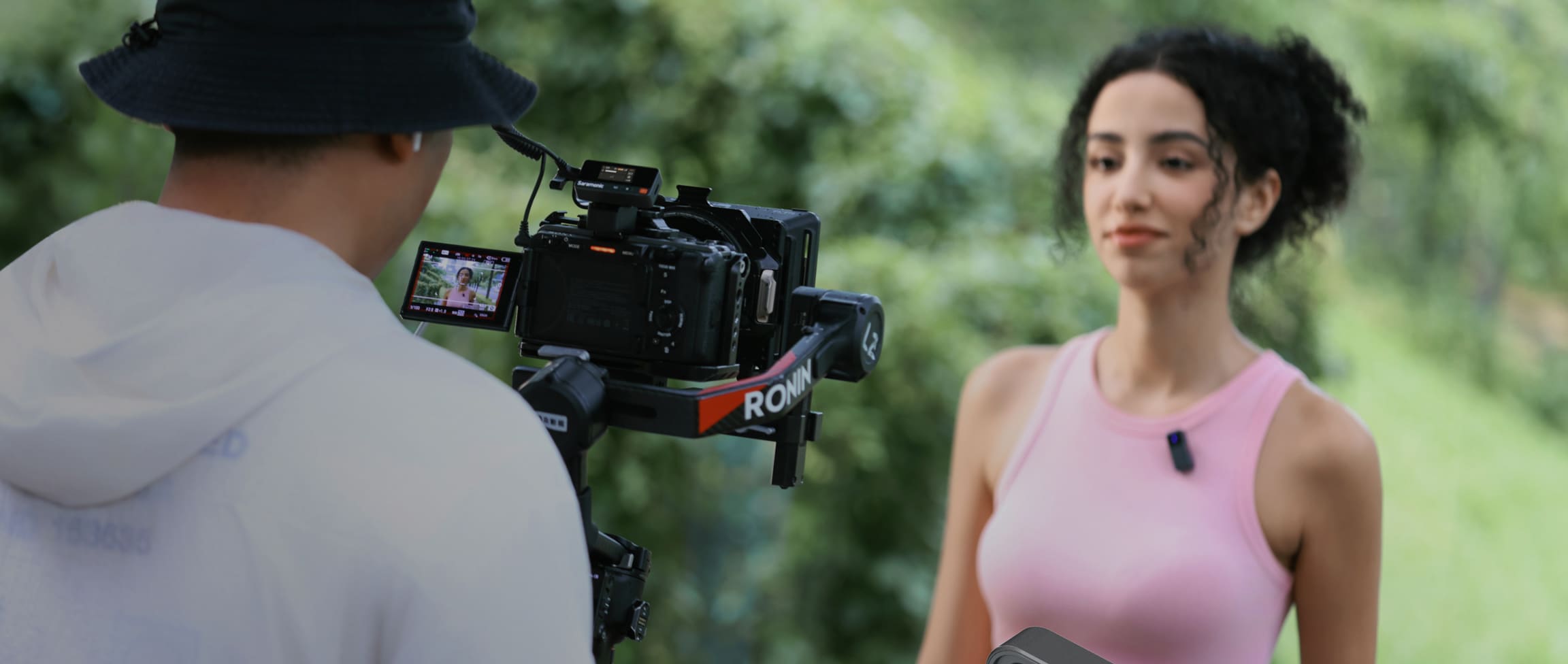 Man filming a woman in pink dress with a professional video camera outdoors