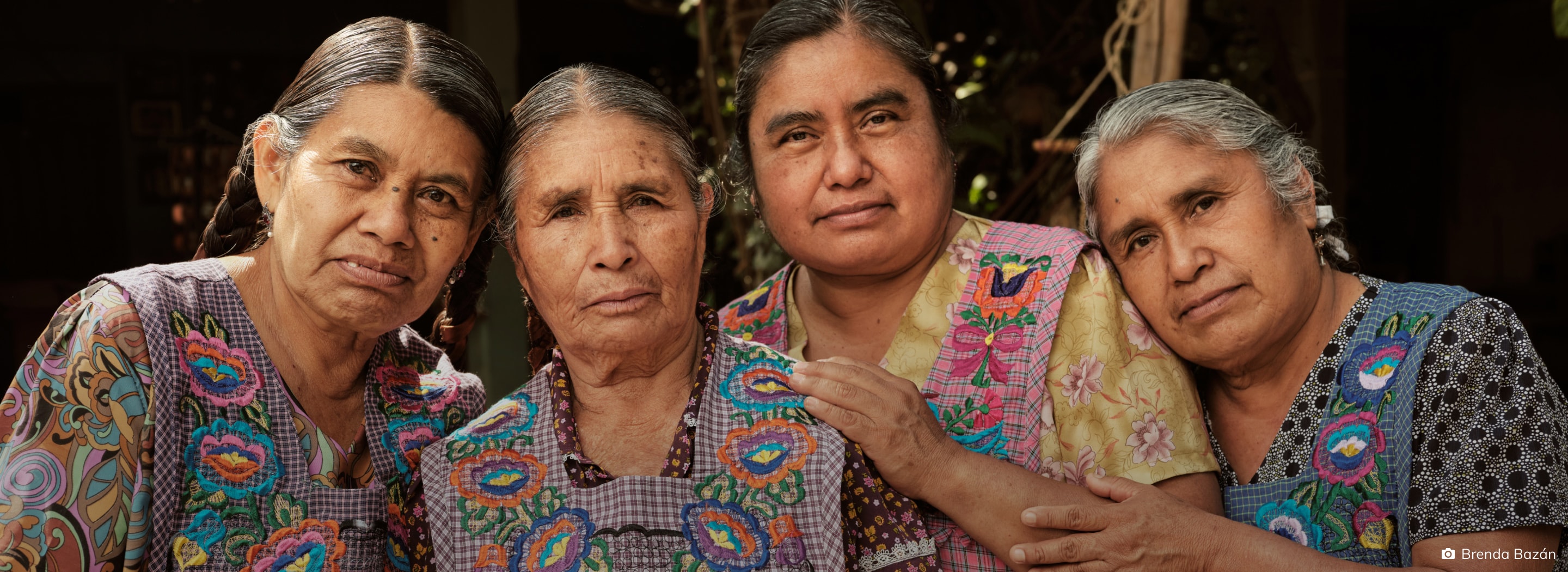Four elderly women in traditional blouses posing closely together