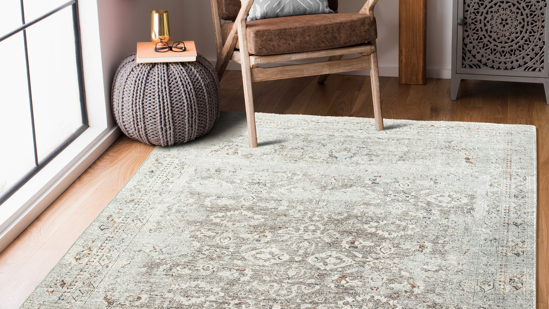 Cozy living room corner with an elegant chair, a stylish round pouf, and a soft patterned area rug near a large window