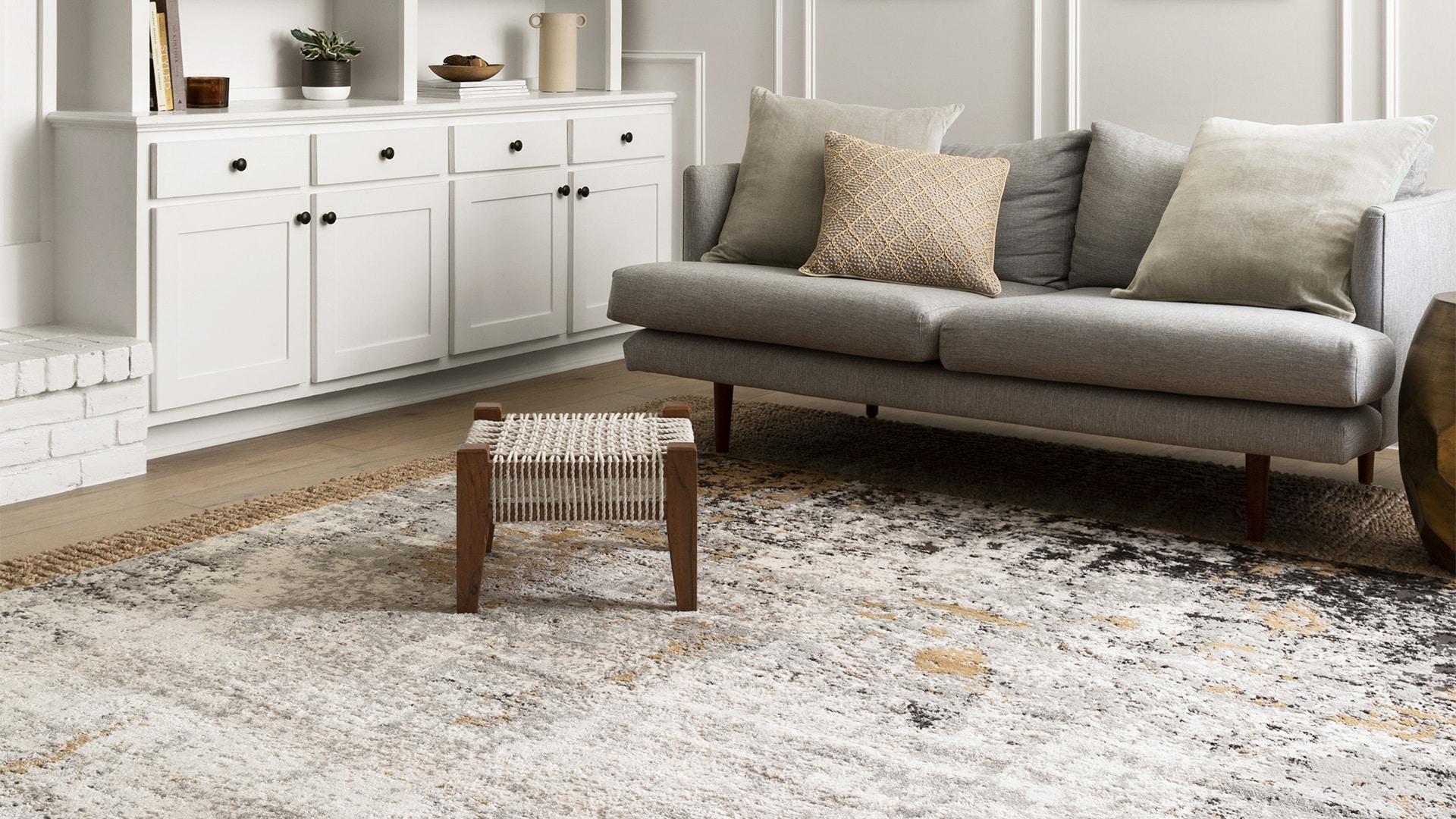 Modern living room with a gray sofa, small wooden stool, white cabinet, and decorative rug