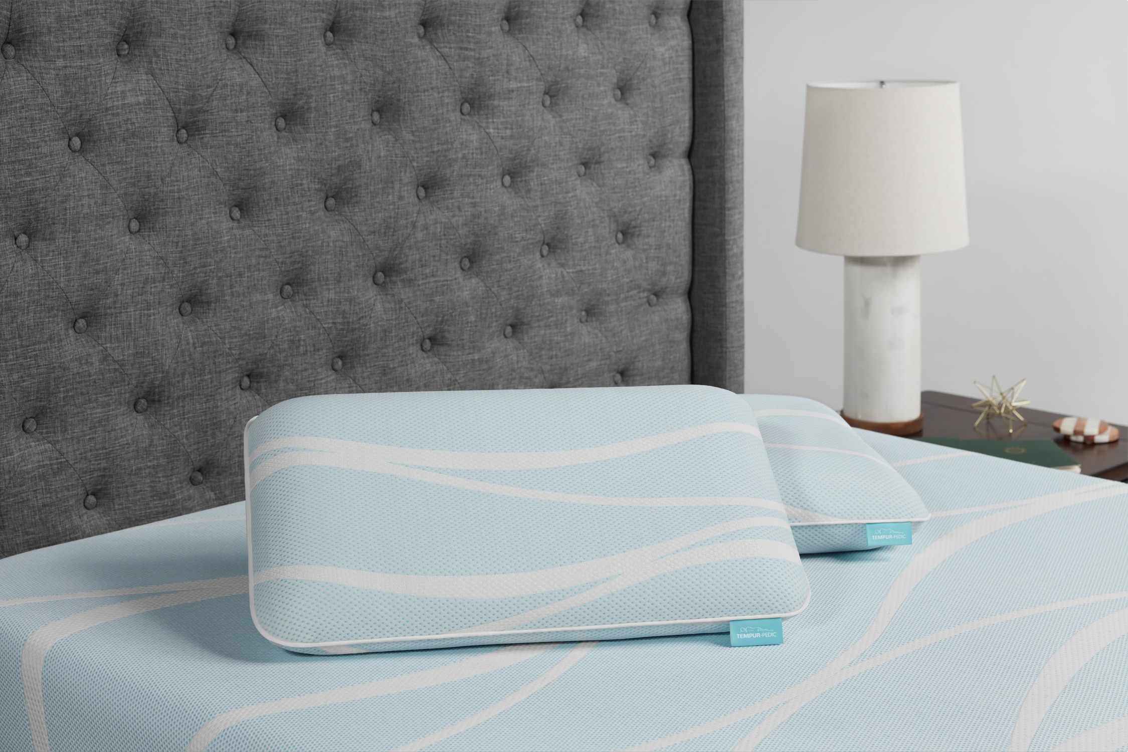 Orthopedic pillow on a neatly made bed with a grey tufted headboard and table lamp