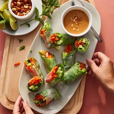 Fresh spring rolls with peanut dipping sauce on a wooden platter