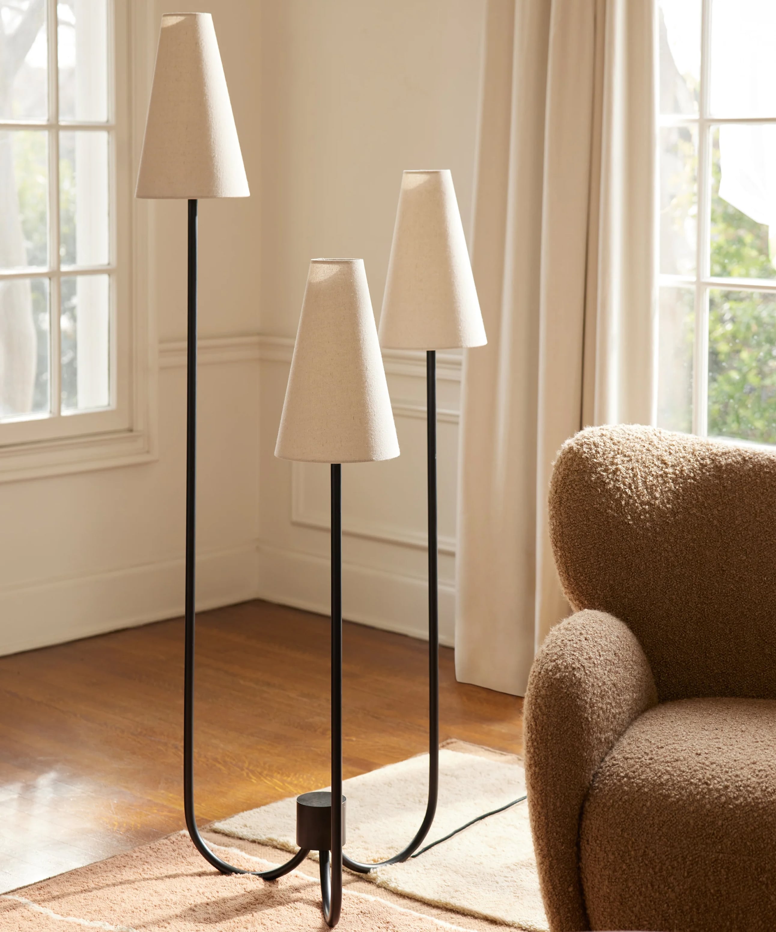 Three shaded floor lamps in a bright room near a brown armchair