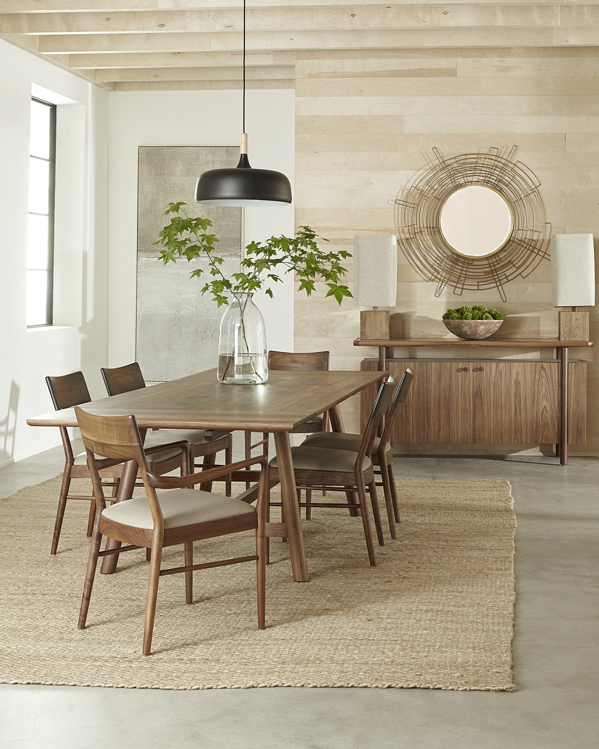 Modern dining room with wooden table, chairs, sideboard, and a circular mirror on textured wall