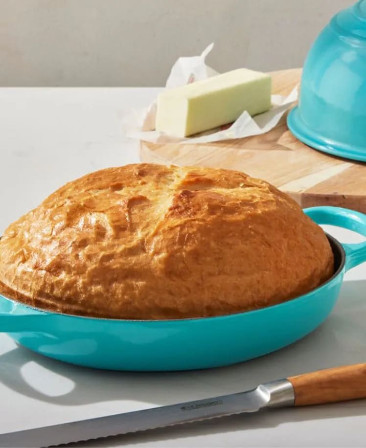 Freshly baked bread in a blue skillet with butter and a blue kettle in the background