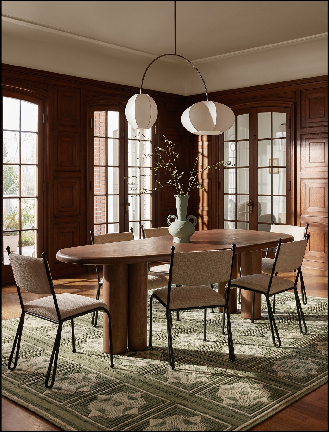 Elegant dining room with oval table, modern chairs, and pendant lights, surrounded by wood-paneled walls