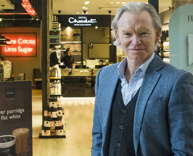 Man in suit smiling in front of a chocolate store in a mall