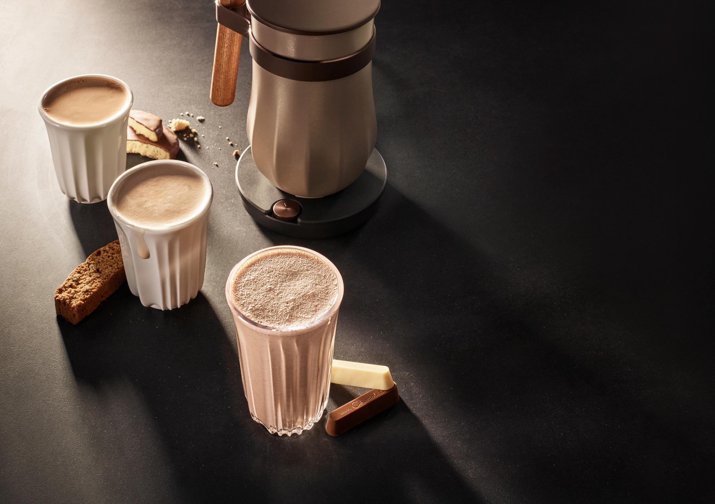 Three cups of coffee with biscuits on a dark surface, illuminated by soft light