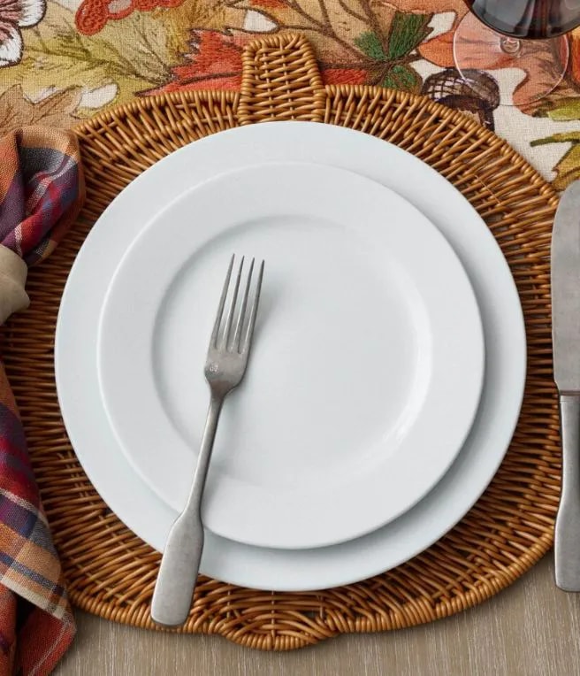 White plate with a fork on a woven placemat, set on a table with a fall-themed cloth