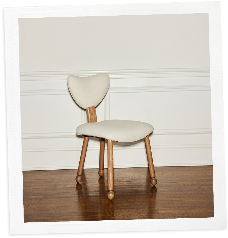 A modern wooden chair with a heart-shaped back and light cushion, against a white paneled wall