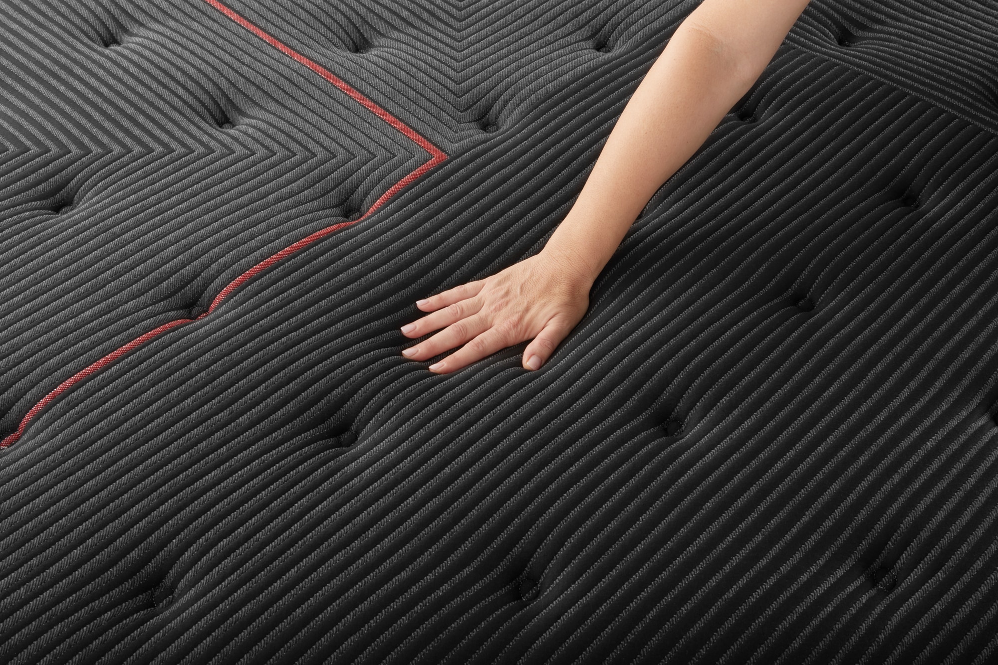Hand touching a textured mattress with black fabric and red stitching