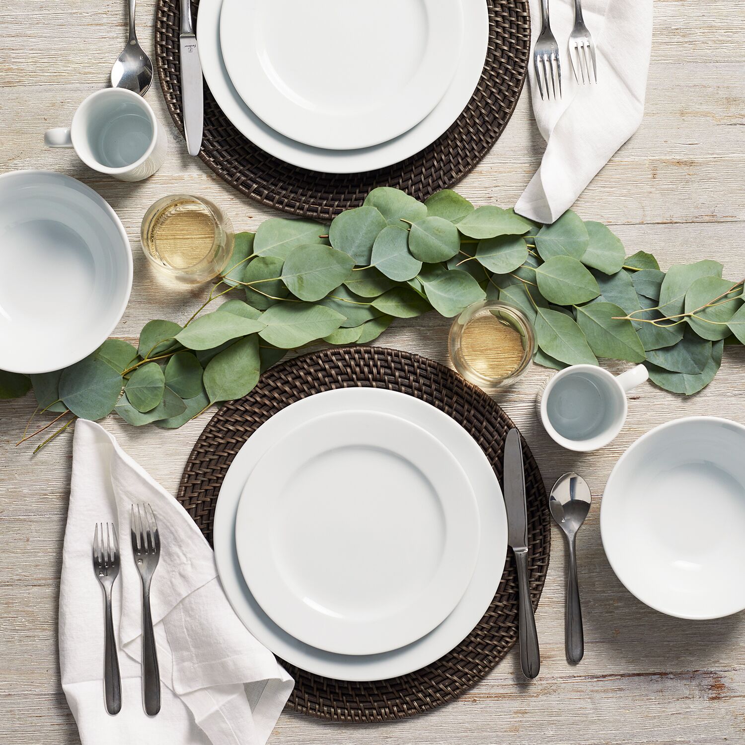 Elegant table setting with white plates, silverware, and eucalyptus garland on a wooden table
