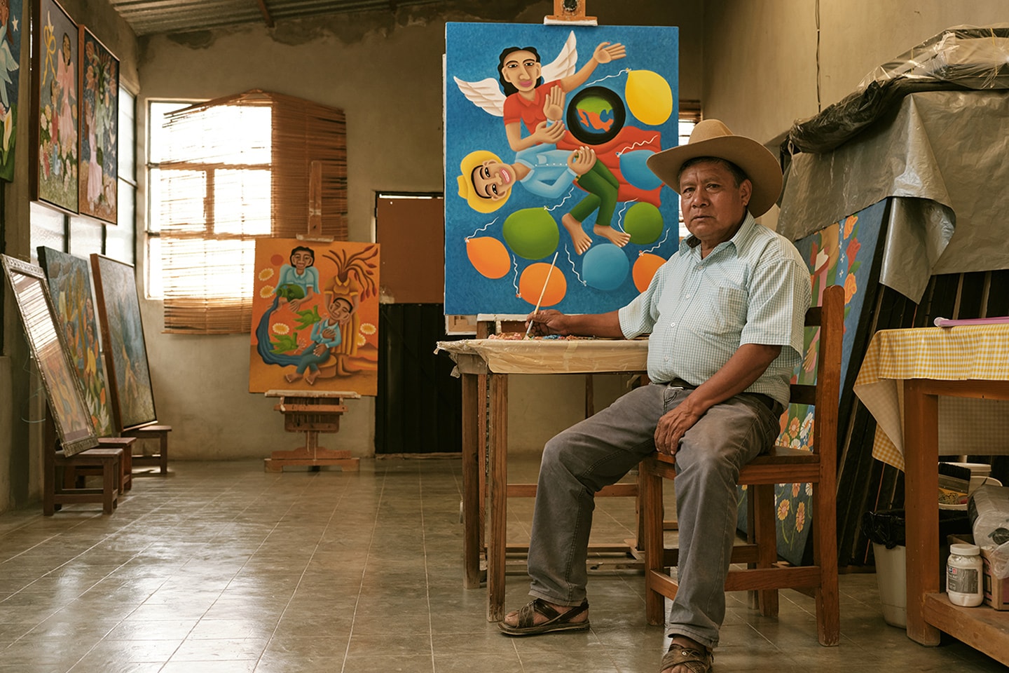 Elderly man sitting in an art studio with colorful paintings, one depicting a vibrant circus scene