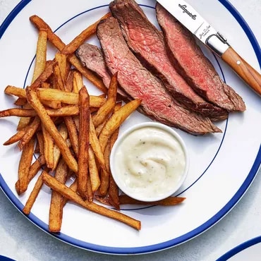 Sliced steak, fries, and sauce on a plate with a steak knife