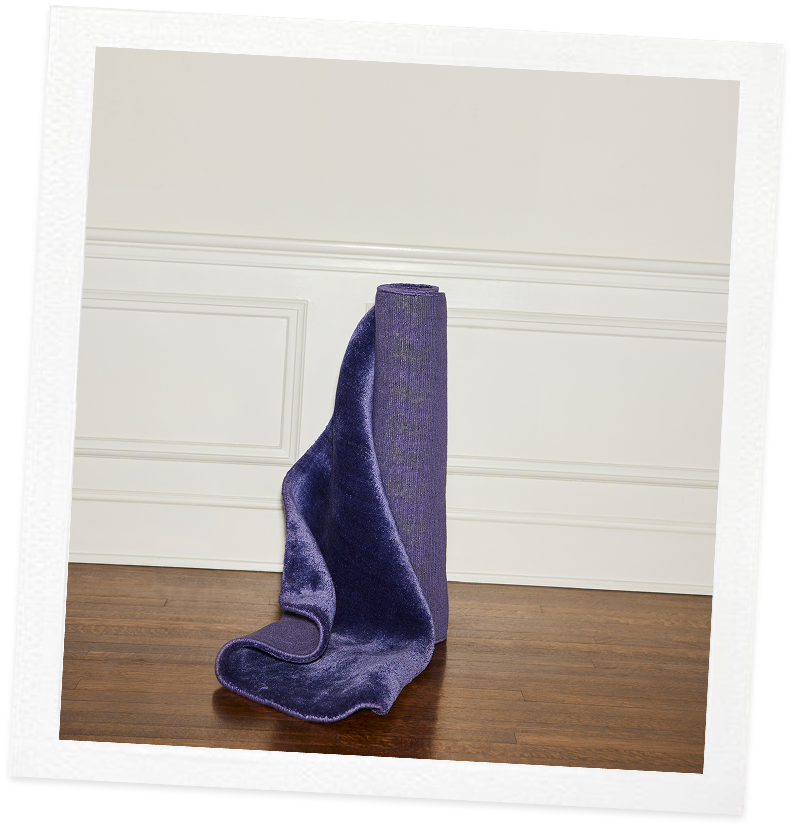 A single purple sock standing upright on a wooden floor against a white wall
