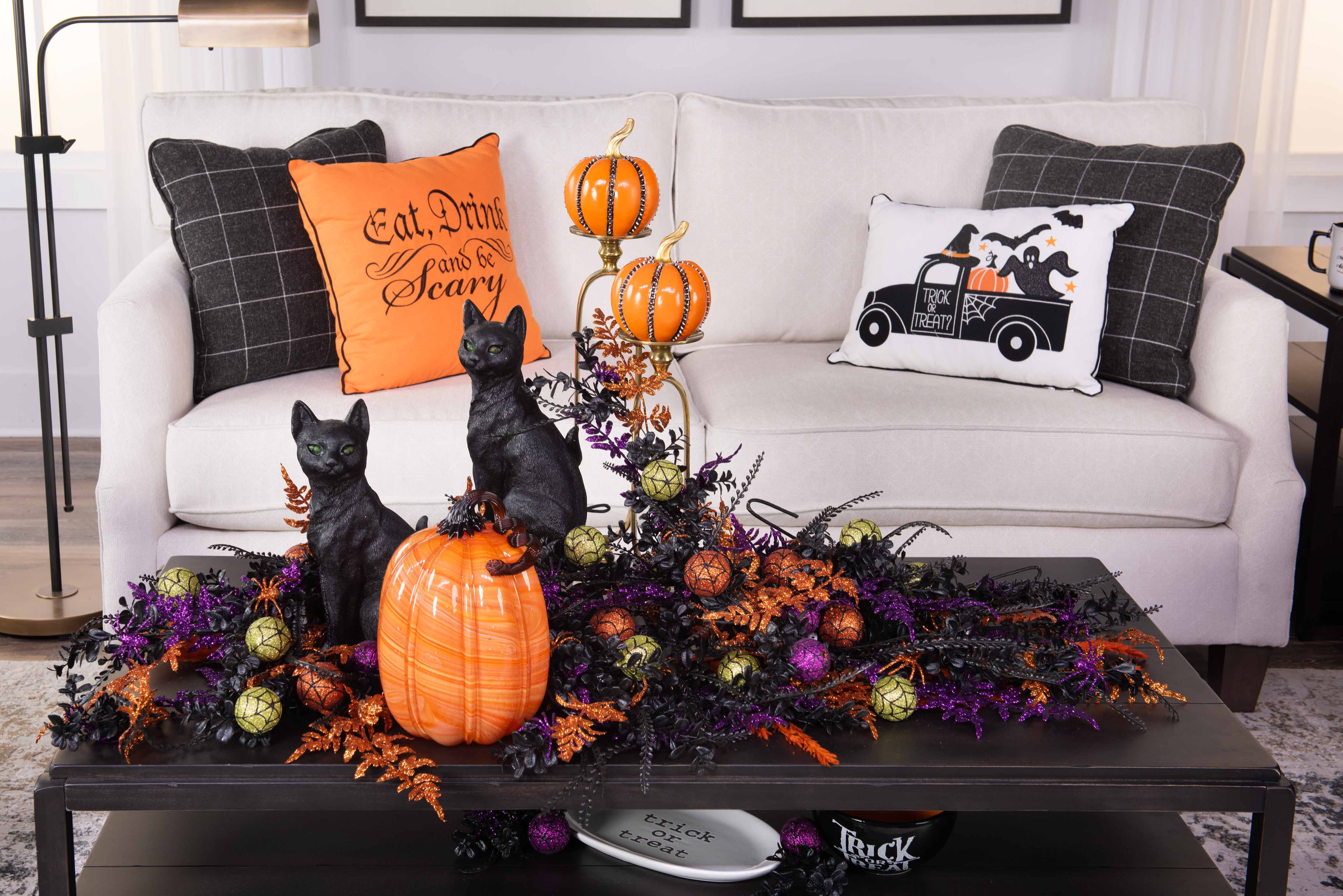 Halloween-themed living room decor with festive pillows, a pumpkin, and black cat figurines on a coffee table