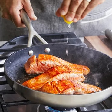 Person cooking salmon fillets in a skillet on a stove