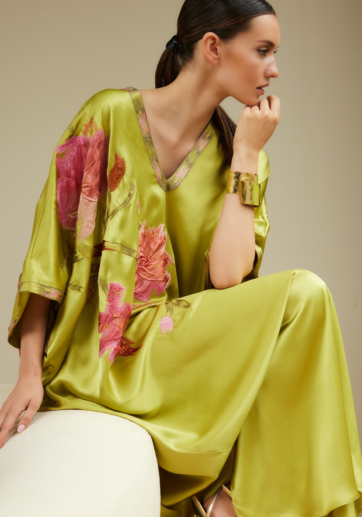 Woman in elegant green silk dress with floral design, posing thoughtfully