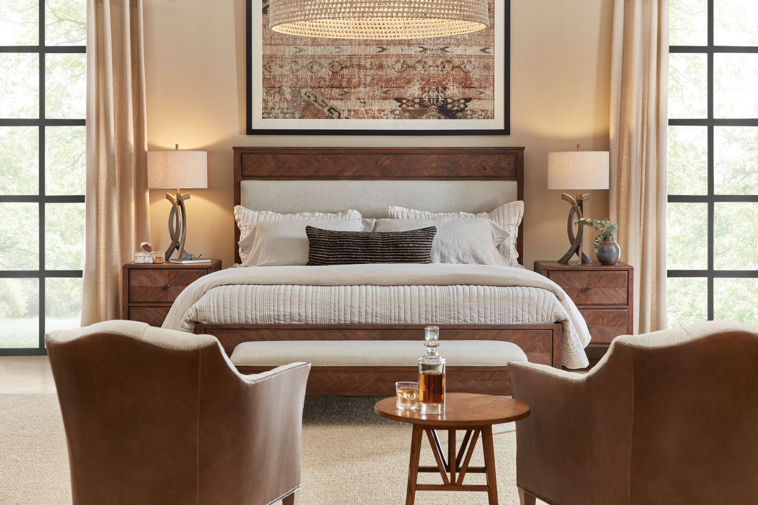 Elegant bedroom with a large bed, two chairs, a small table and wall art between windows