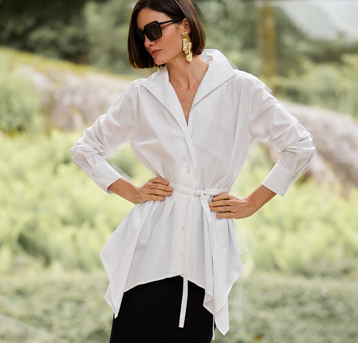 Woman in sunglasses and white blouse posing outdoors