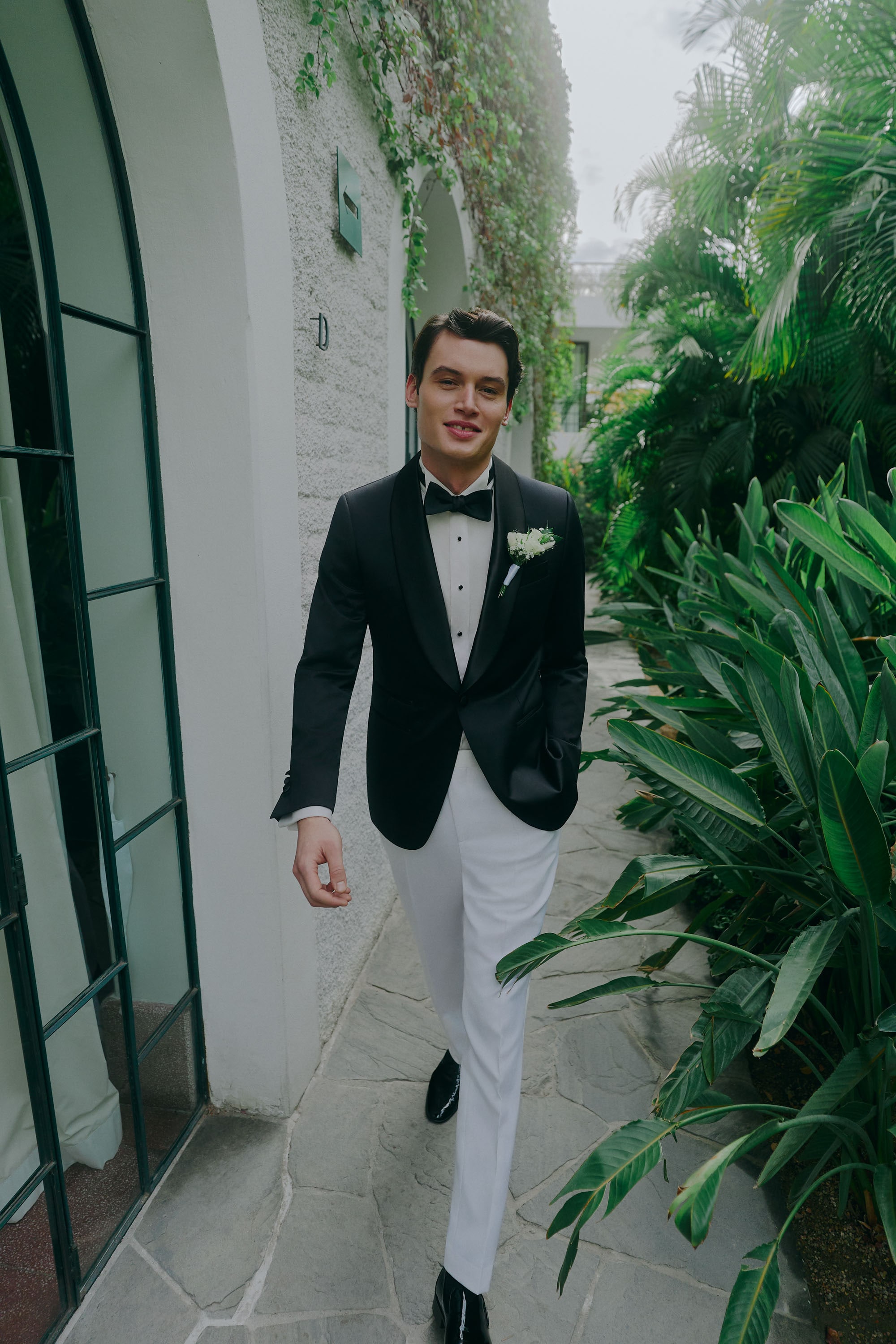 Man in tuxedo with bow tie walking through garden pathway