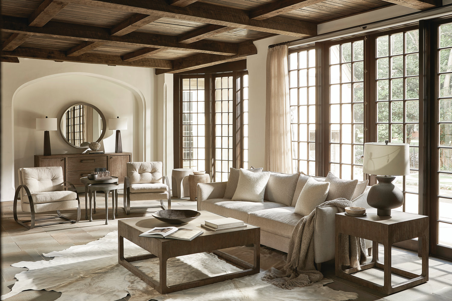 Elegant living room with neutral tones, beamed ceiling, large windows, and stylish furniture