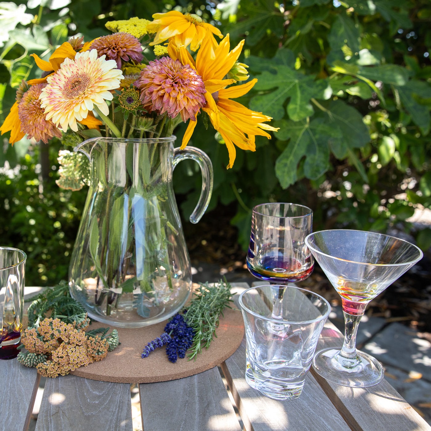 Sunflowers and mums in a pitcher on a table with wine glasses and grapes