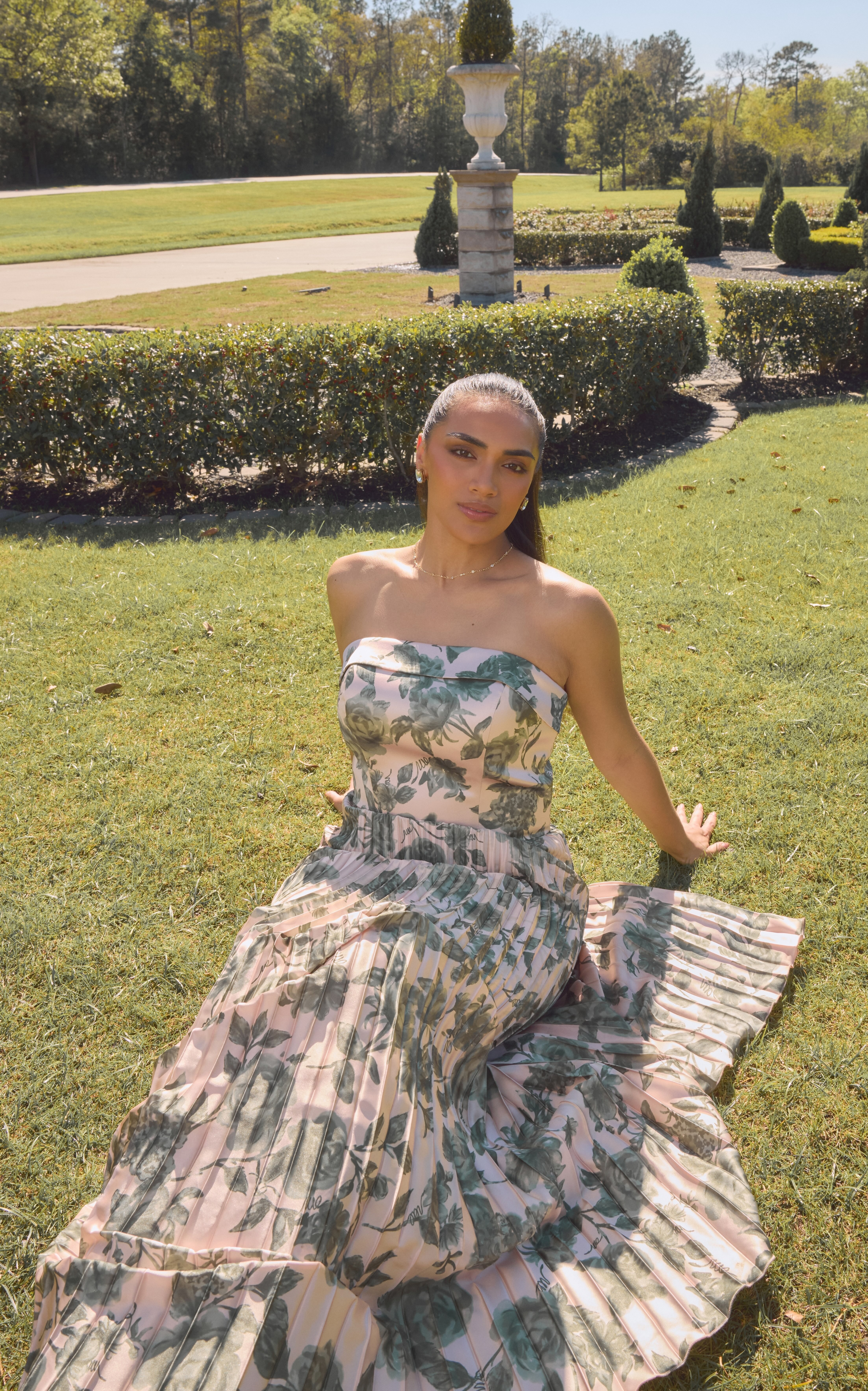 Woman in a floral dress sitting on grass in a sunny garden