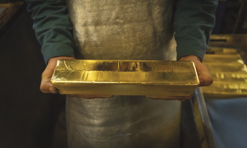 Worker in apron holding a golden bar.