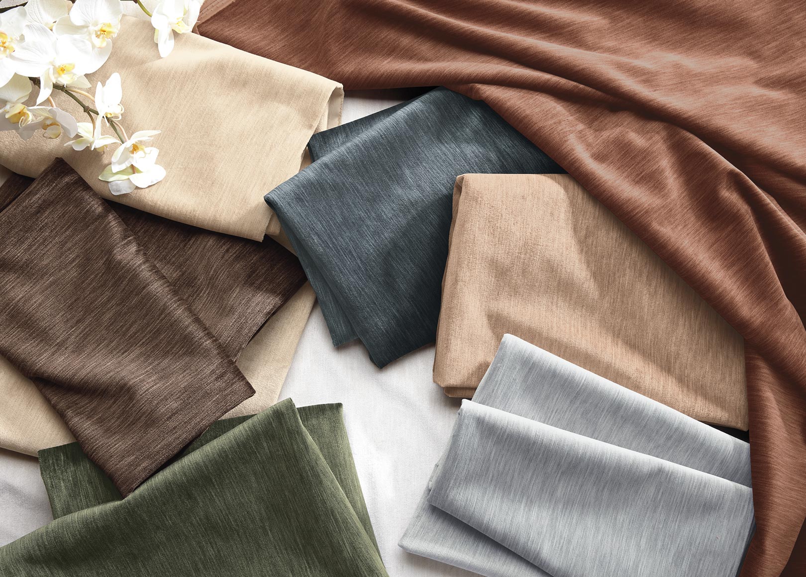 Assorted fabric swatches in various colors and textures, spread out with some white flowers