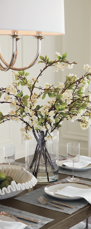 Elegant dining table setup with cherry blossoms in a glass vase under a stylish chandelier