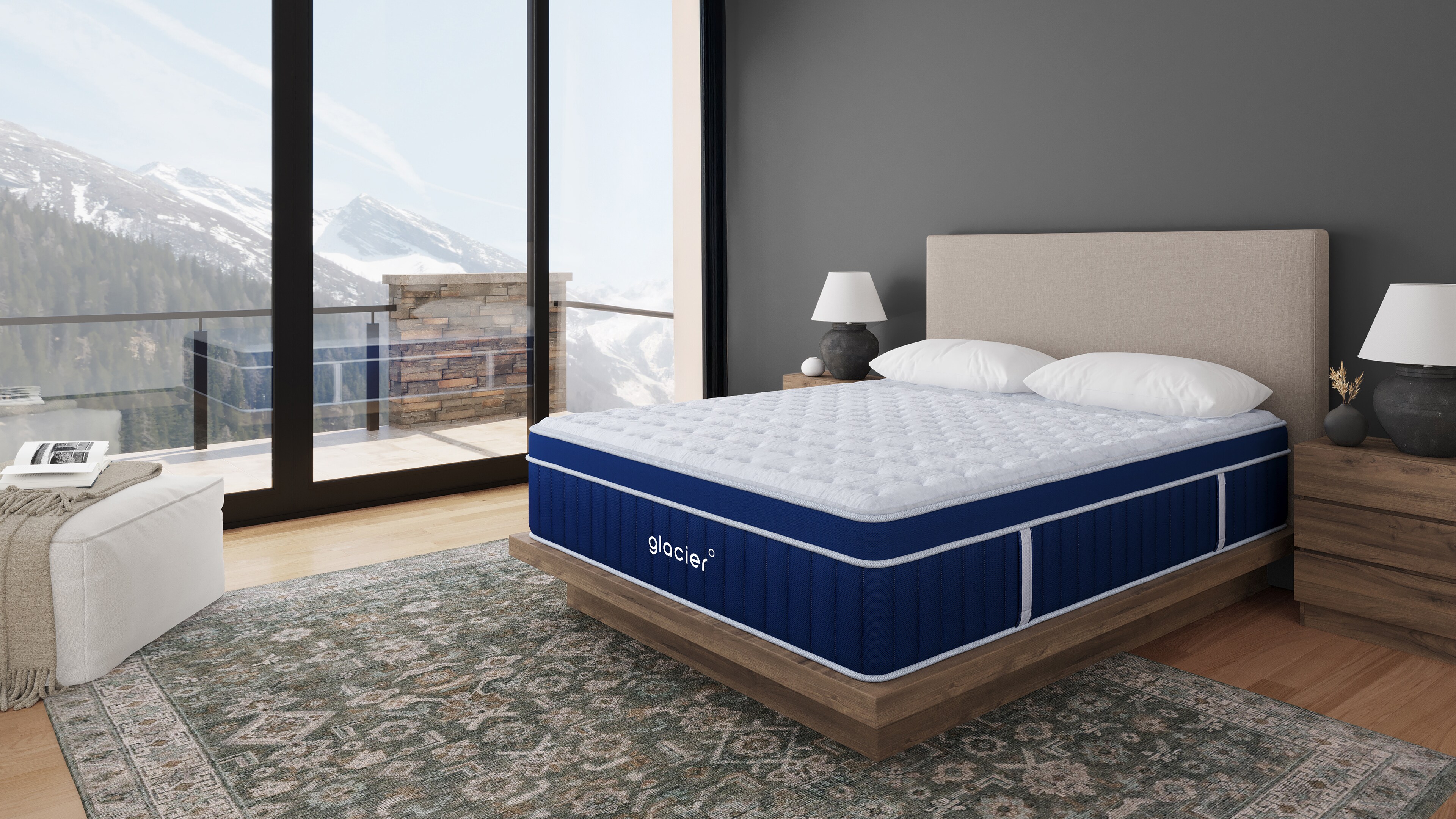 Modern bedroom with a large blue and white bed, area rug, and panoramic mountain view through floor-to-ceiling windows