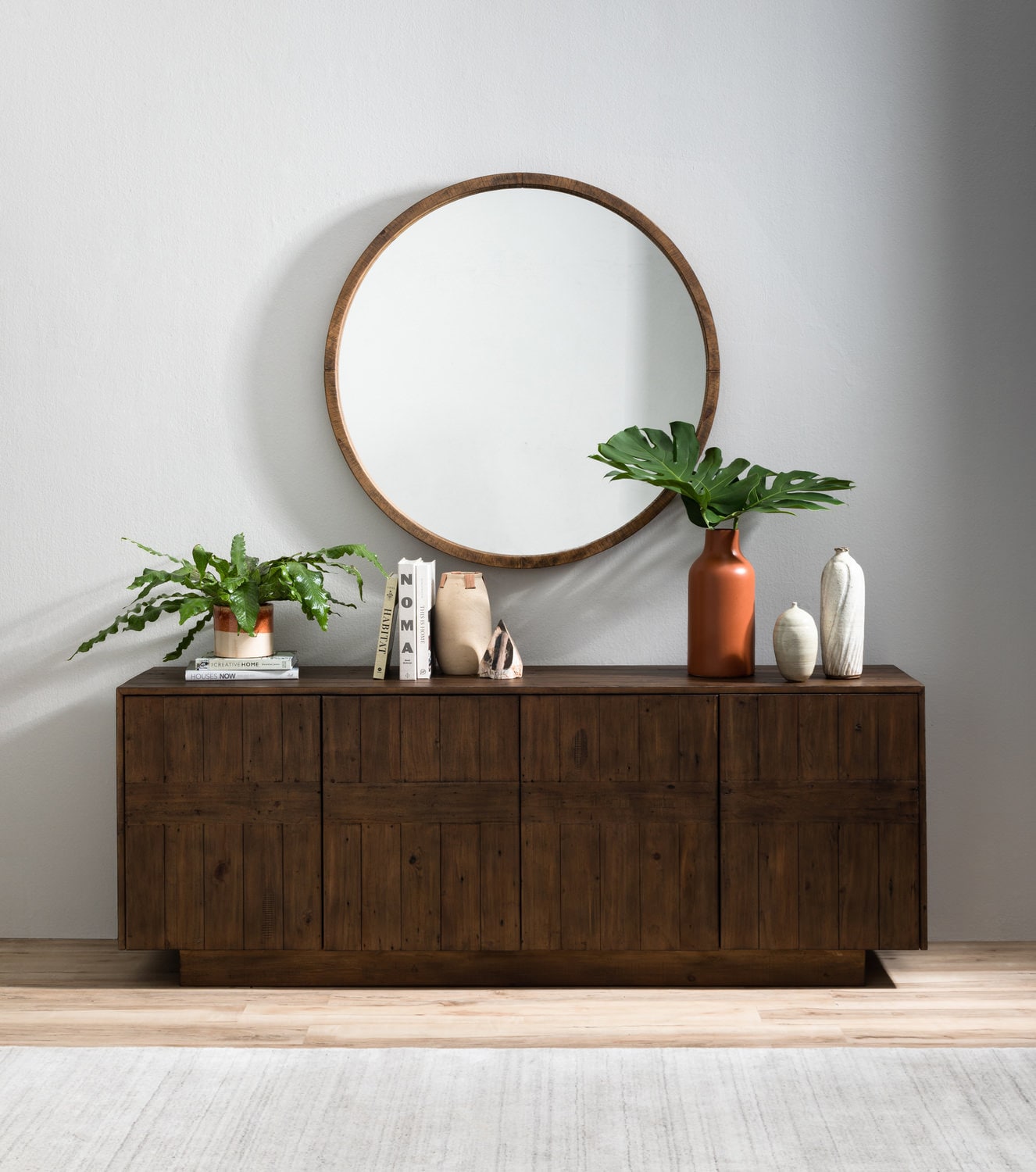 A wooden sideboard with decorative items and a round mirror on a wall
