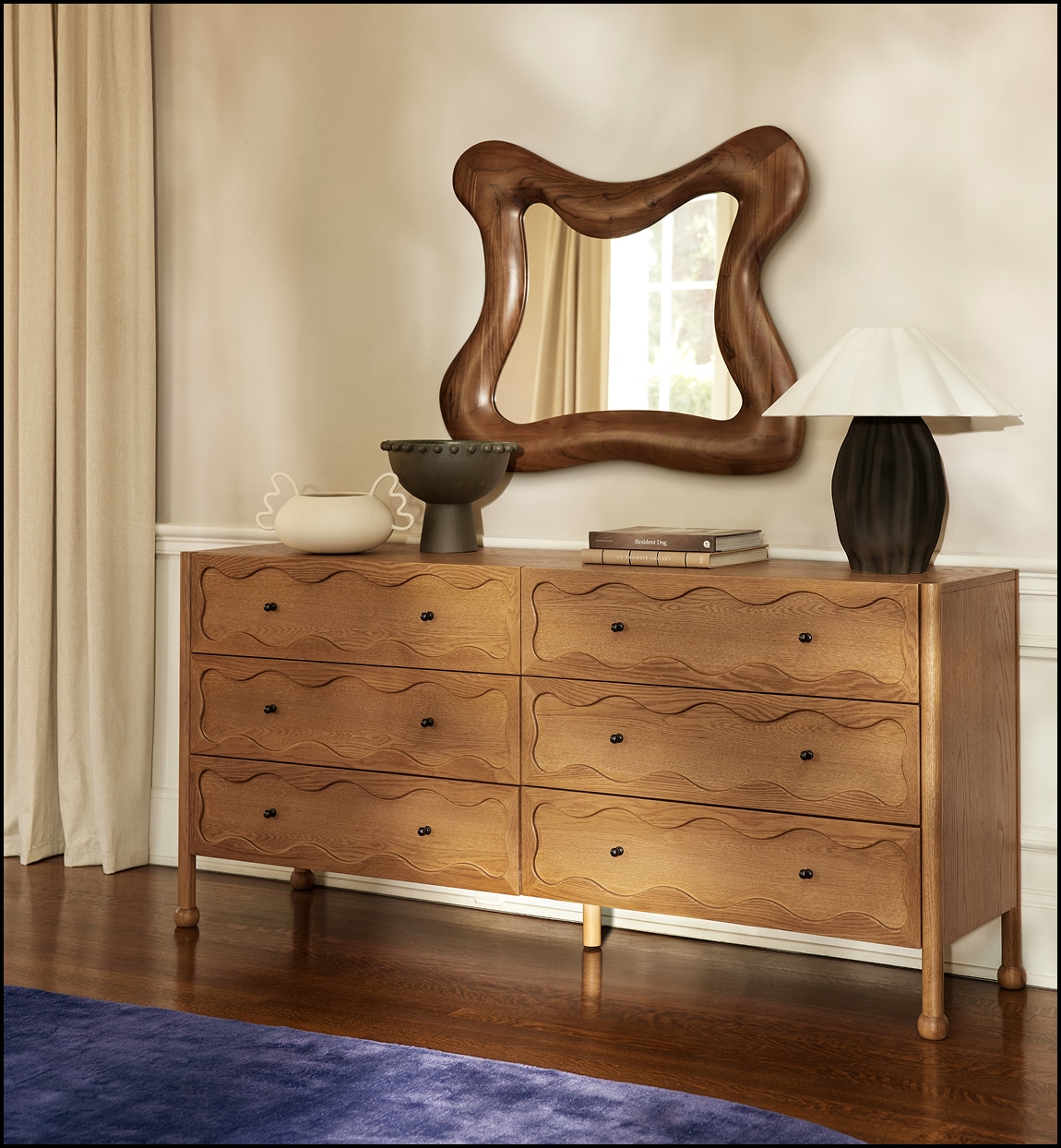 Wooden dresser with sculpted drawers and an irregular mirror above it in a room