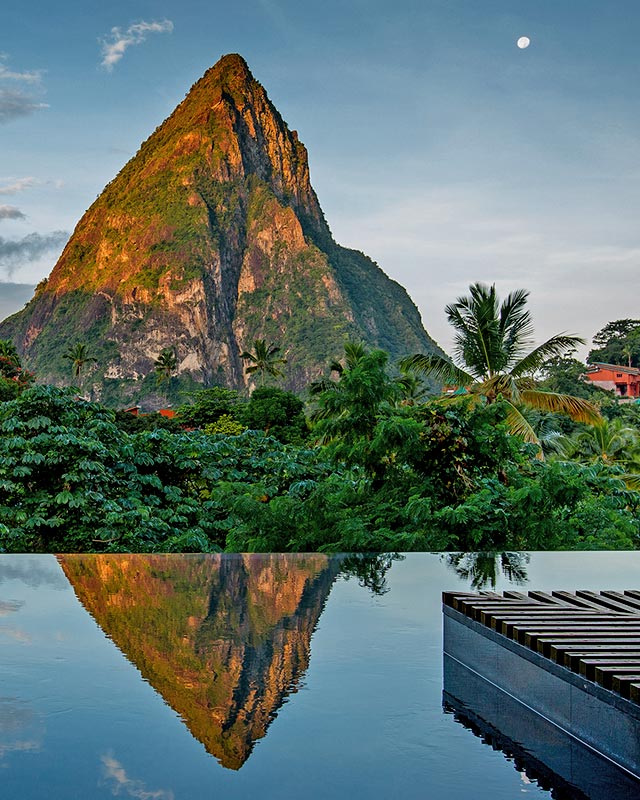 Mountain peak with lush greenery reflected in a tranquil water surface at twilight