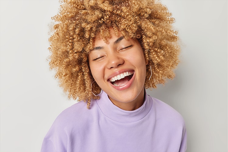 Joyful woman with curly hair laughing, wearing a purple turtleneck